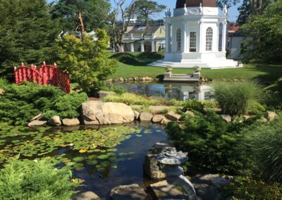 A design by 18th century English architect James Paine inspired the footbridge welcoming visitors to the lily pond. In the background, the octagonal structure with a cupola is based on an original design by Samuel McIntyre for a church in Salem, MA.